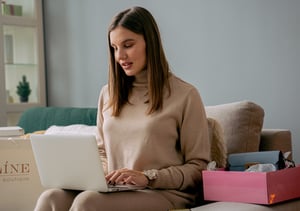 Woman sitting on a grey couch while working on a laptop computer.