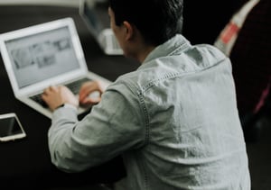 Man in a grey shirt working on a laptop computer.