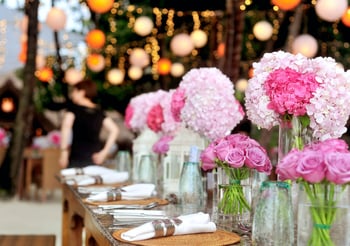 Pink flowers in vases on a long wedding table setting.