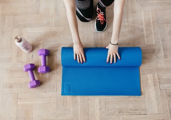 Person rolling up a blue yoga mat next two a water bottle and two purple dumbells.