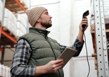 Man in a vest and beanie scanning packages to be shipped.