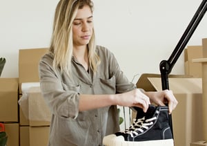 Woman putting cardboard shoe inserts in a pair of black and white high top sneakers.