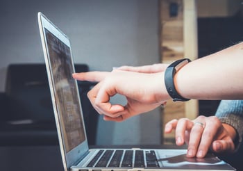 Two people pointing to a laptop screen.