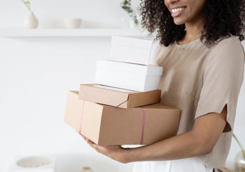 Woman holding four cardboard boxes.