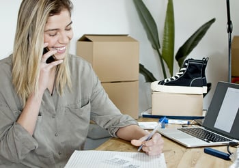 Woman on the phone writing a note on a piece of paper.