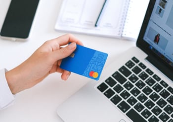 Person holding a blue credit card next to a laptop computer.