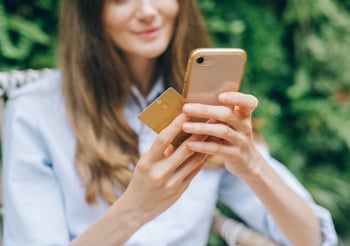 Person holding a gold credit card while looking at their smartphone.