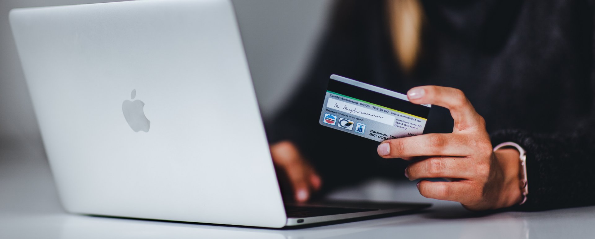 Person holding a credit card next to a laptop.