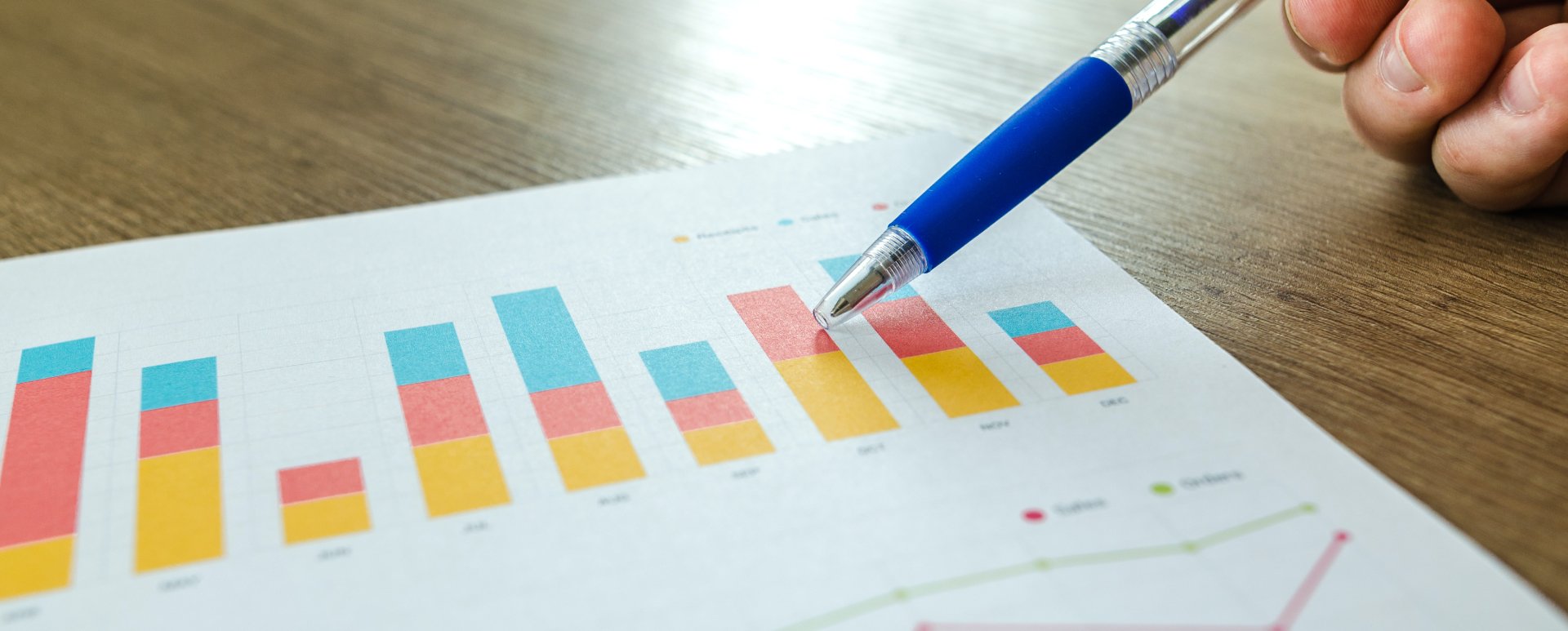 Person pointing to a bar graph with a pen.