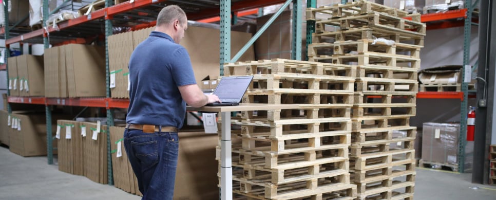 Person standing next to a stack of wooden pallets working on a laptop.